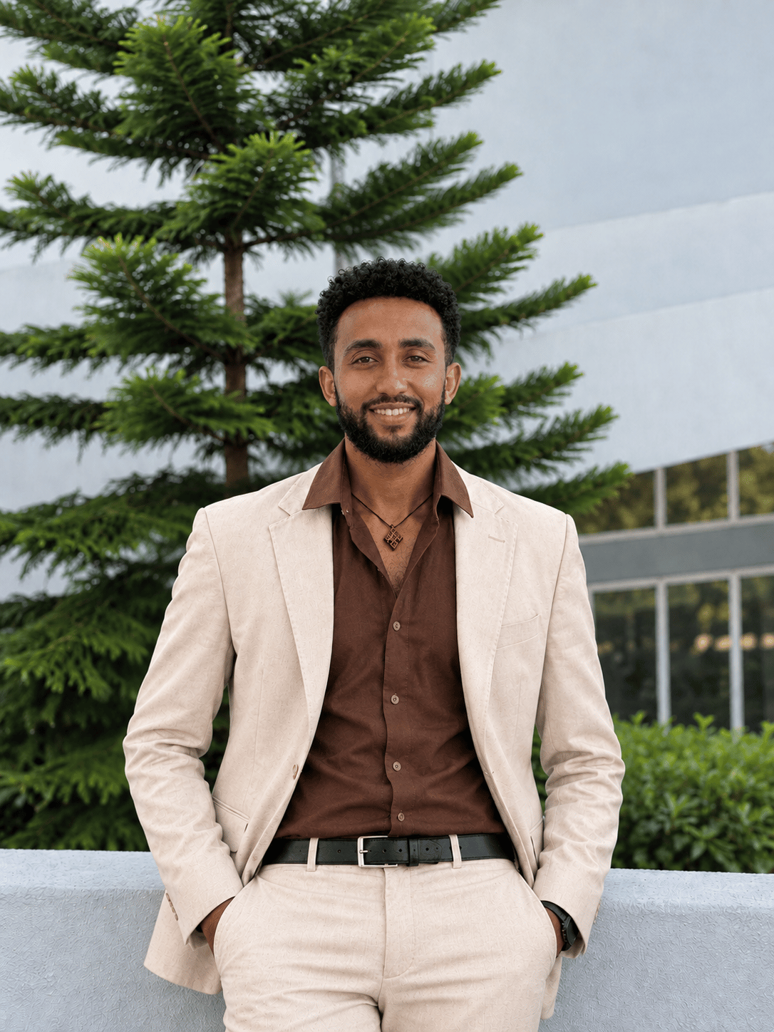 Abel Addis in a beige blazer and brown shirt, smiling, with his hands in his pockets